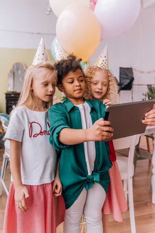 Free Three young girls at a birthday party taking a group selfie with a tablet, having fun. Stock Photo