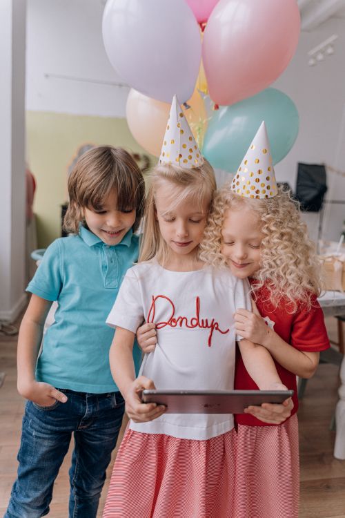 Free Three children enjoying a virtual birthday celebration with balloons and party hats. Stock Photo