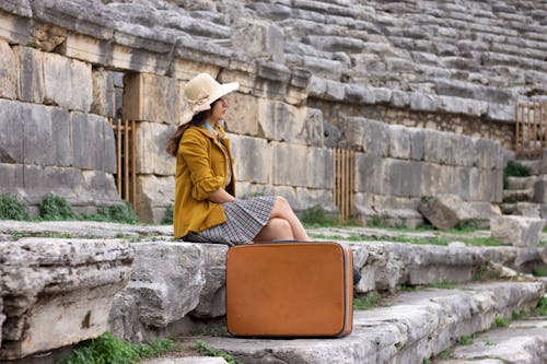 Woman in Wide Brimmed Hat and with Suitcase Sitting on Concrete Steps