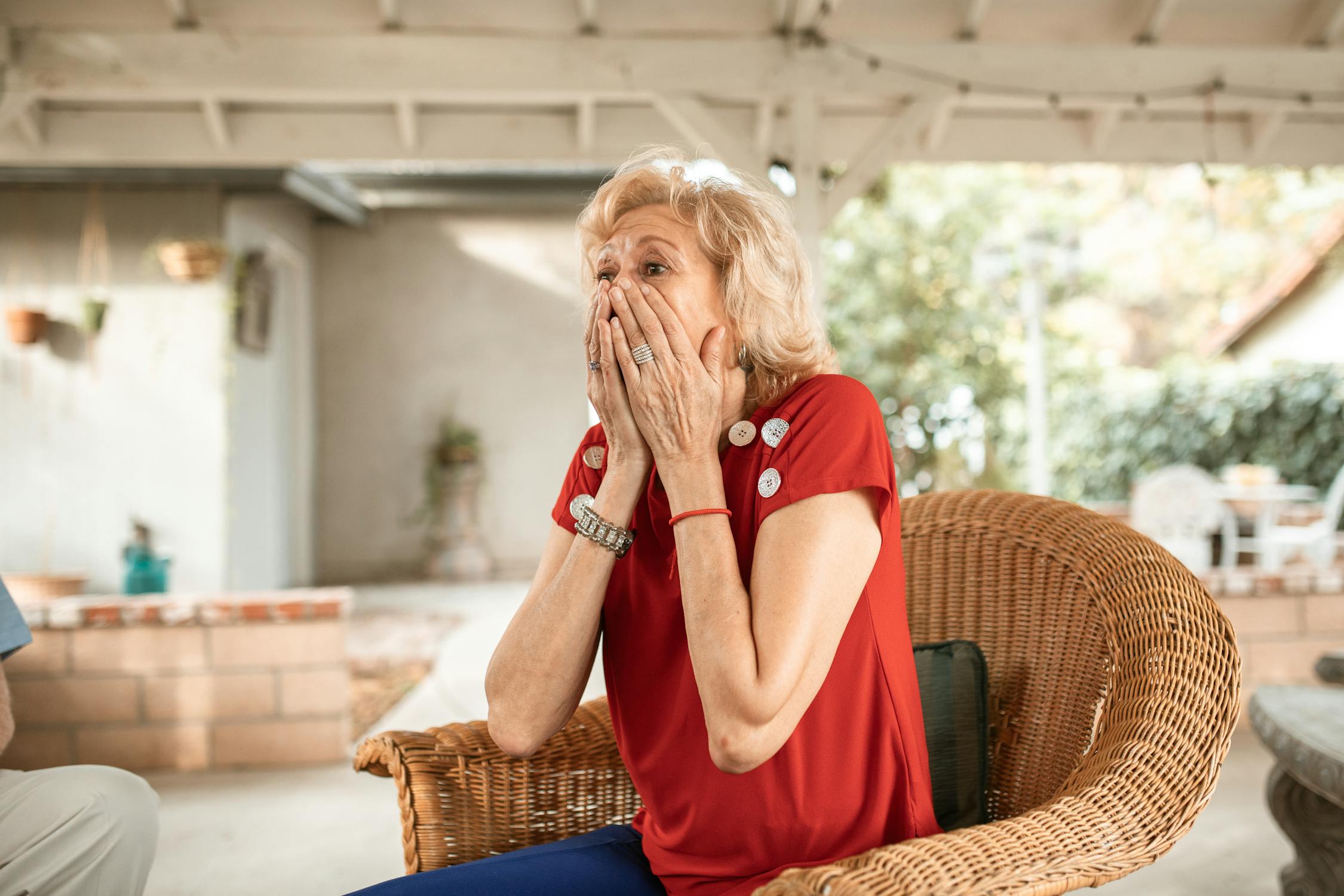 Surprised Woman in Red Shirt Sitting on Wicker Armchair