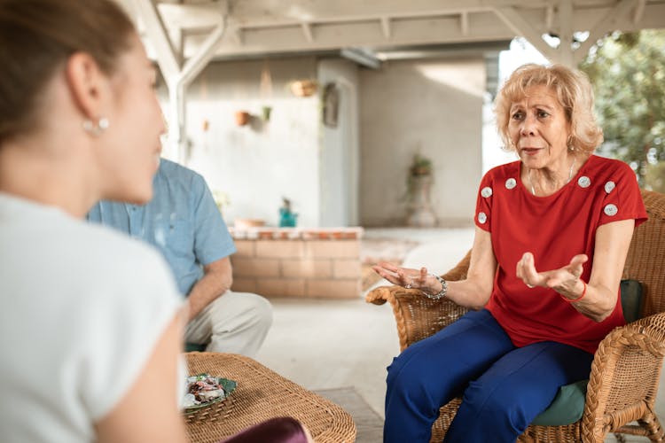 An Elderly Woman Sitting On A Woven Chair While Talking To Her Daughter