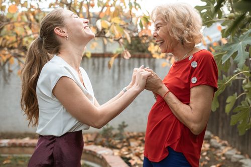 Free A joyful exchange between two women, young and senior adult, holding hands and laughing outdoors. Stock Photo