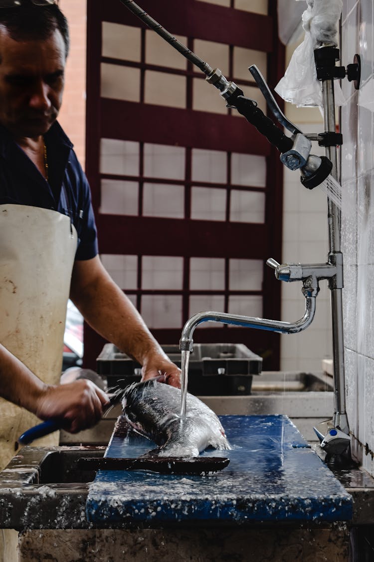 Man In Blue And White Polo Shirt Removing Fish Sclaes