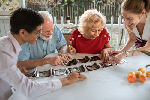 Free An elderly couple with family happily viewing ultrasound pictures at a table indoors. Stock Photo