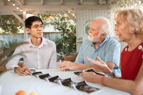 Free Senior couple and family member discussing ultrasound photos at an outdoor table. Stock Photo