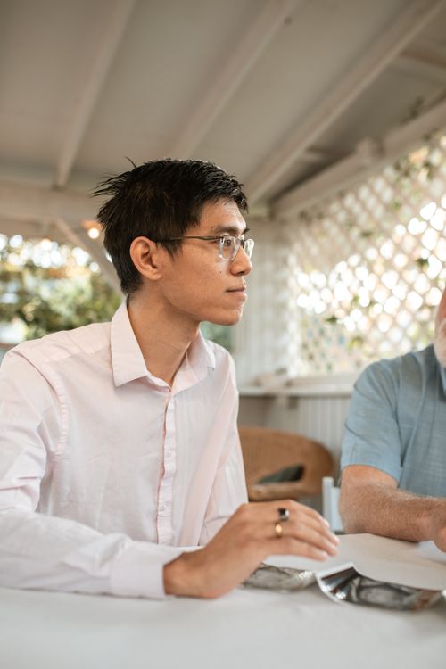 Free Man in thoughtful discussion indoors, seated at a table during the day. Stock Photo