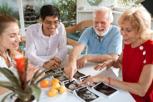 Free Four adults joyfully review ultrasound images at a table, celebrating a new family arrival. Stock Photo