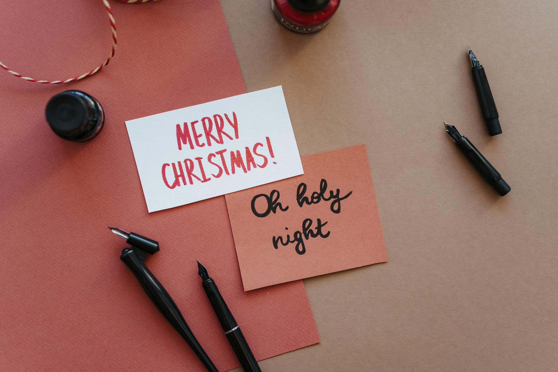 Elegant flat lay of handwritten Christmas cards with fountain pens and ink.