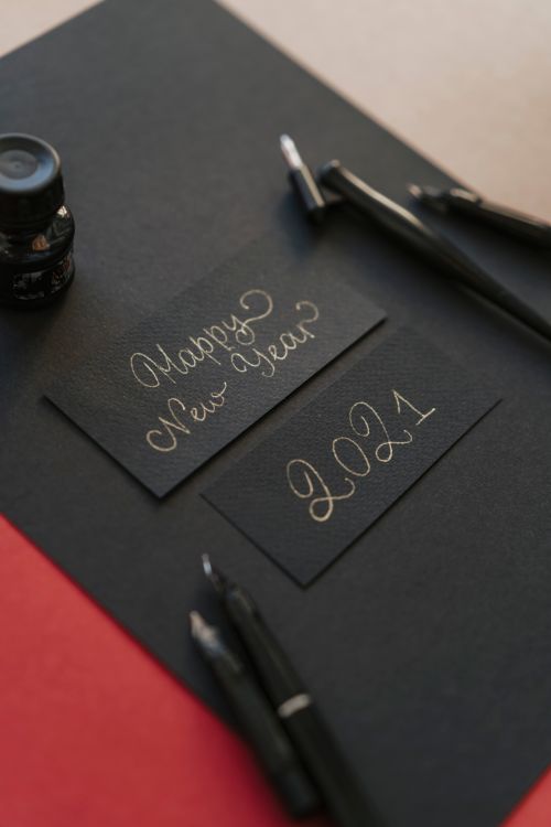 Free Black paper with 'Happy New Year 2021' in gold ink, featuring fountain pens and ink bottle. Stock Photo