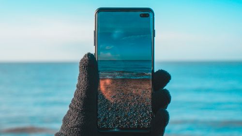 Free Smartphone displaying beach and ocean view on screen at sunset. Stock Photo