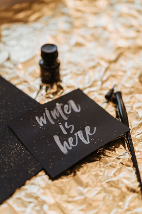 Free Stylish winter-themed calligraphy card with ink pen on shimmering gold backdrop. Stock Photo