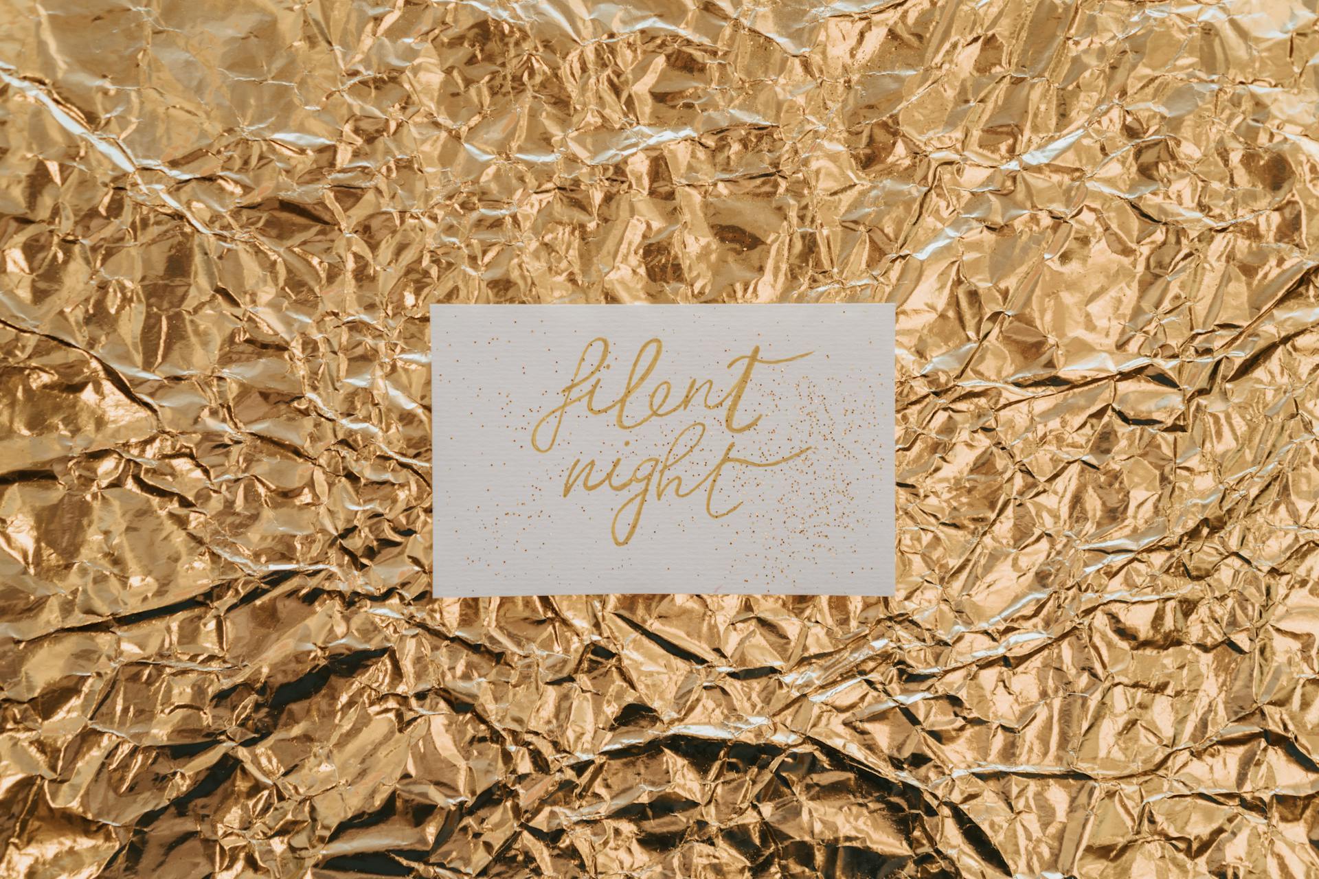 Elegant card with calligraphy text 'silent night' on a crumpled gold foil background, perfect for holiday themes.