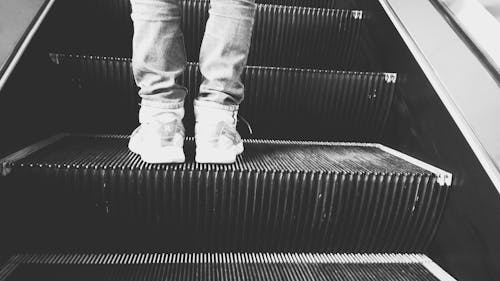 Grayscale Photo of Person Standing on Esclator