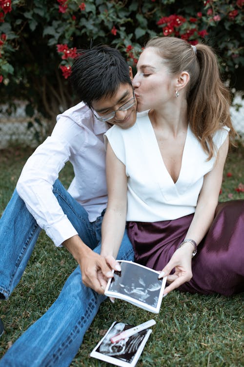 Free Couple Sitting on the Grass Holding Ultrasound Result Stock Photo