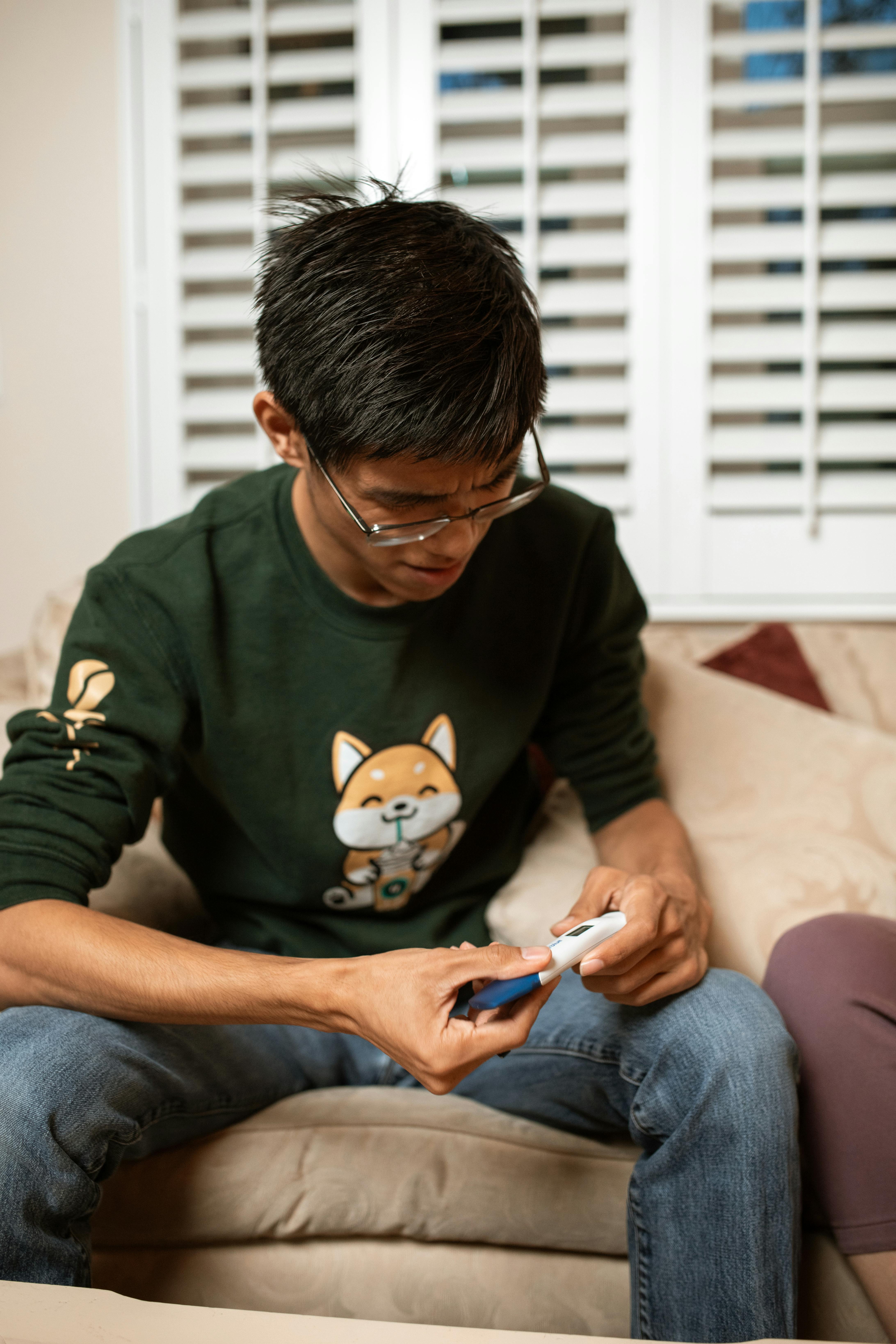 boy in green and black sweater and blue denim jeans sitting on bed