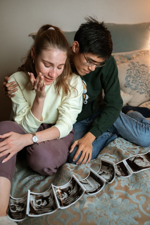 Free Couple sitting on bed, sharing an emotional moment over ultrasound images of their unborn child. Stock Photo