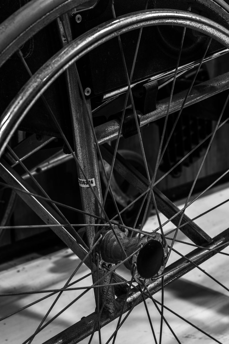 Detailed black and white close-up showing the wheel and spokes of a wheelchair