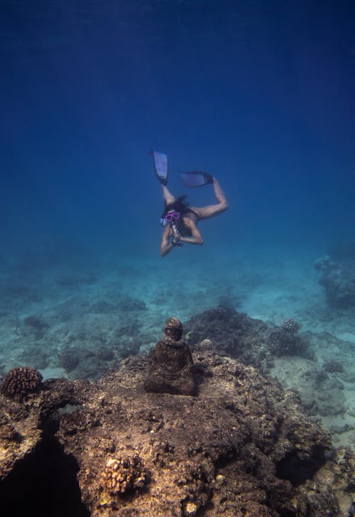 Unrecognizable woman diving underwater above coral