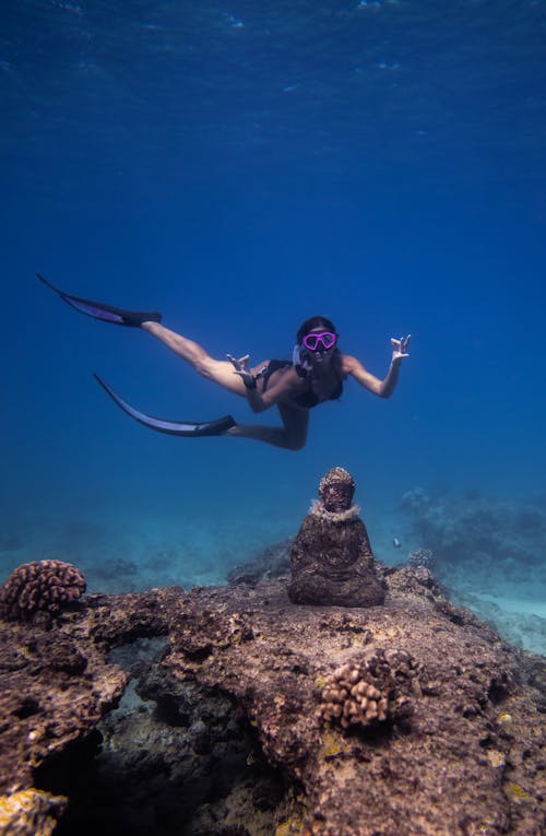 Free Full length of unrecognizable female in mask and flippers diving underwater in and showing Mudra gesture with Buddha on coral rock Stock Photo