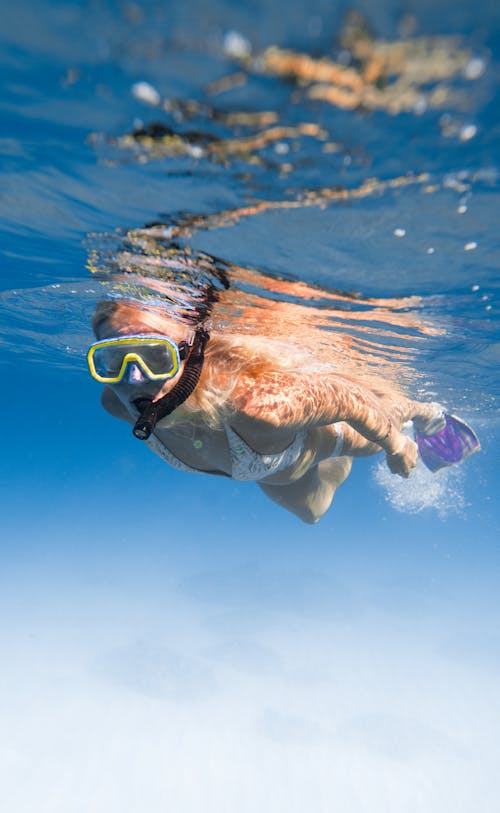 Full length of faceless female diving underwater in bikini and flippers with snorkeling mask in clear blue water