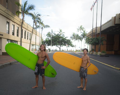 Positive teens in swimwear carrying surfboards in street