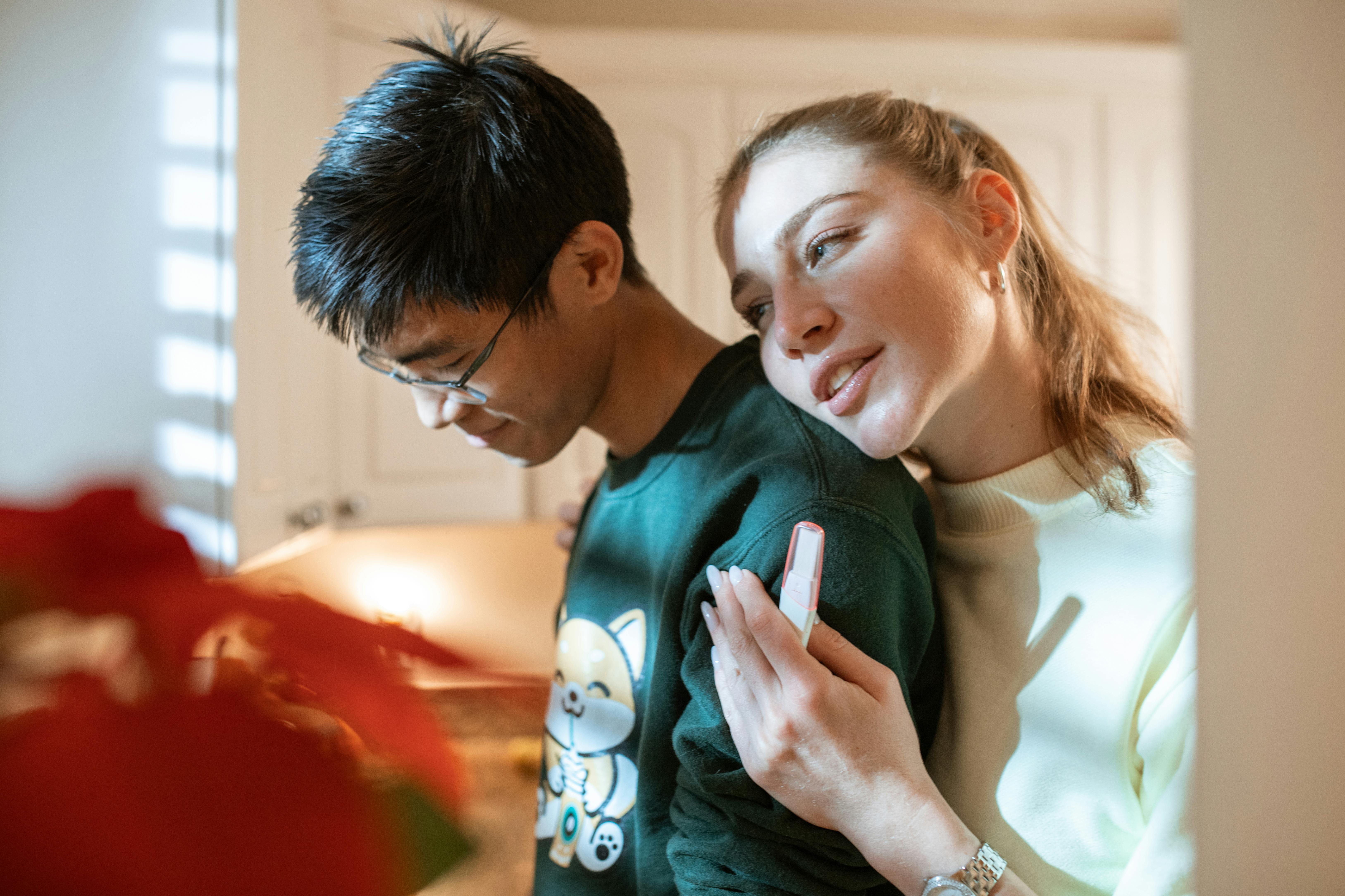 woman in white and black shirt holding smartphone beside man in green crew neck shirt