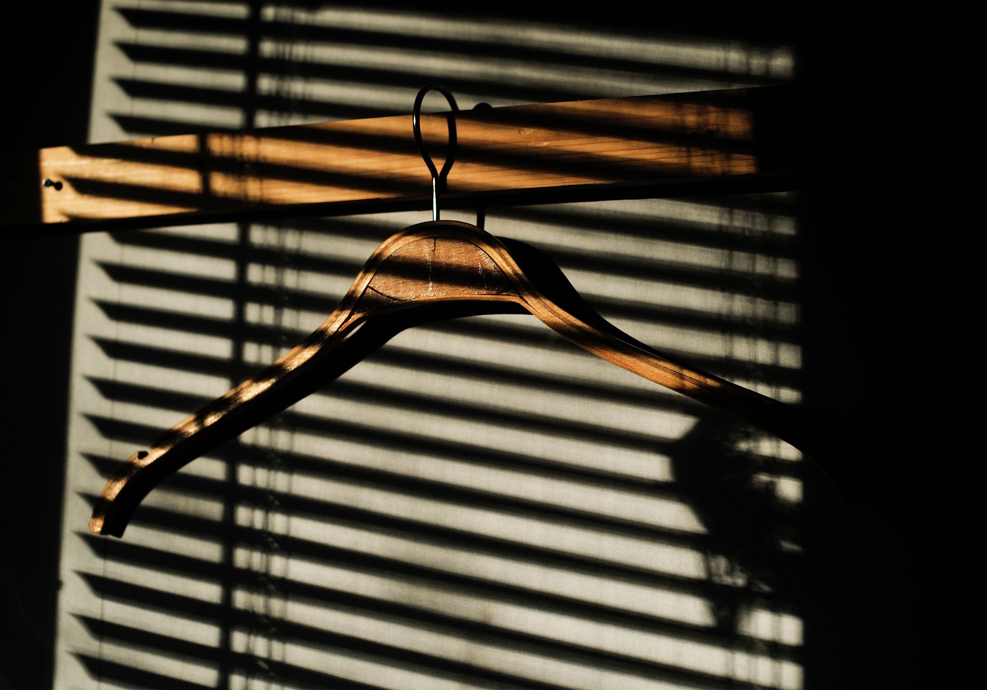 A wooden clothes hanger casts dramatic shadows through blinds in soft light.