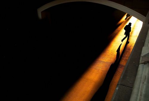 Free Silhouette of a man walking through a dimly lit tunnel, casting long shadows. Stock Photo
