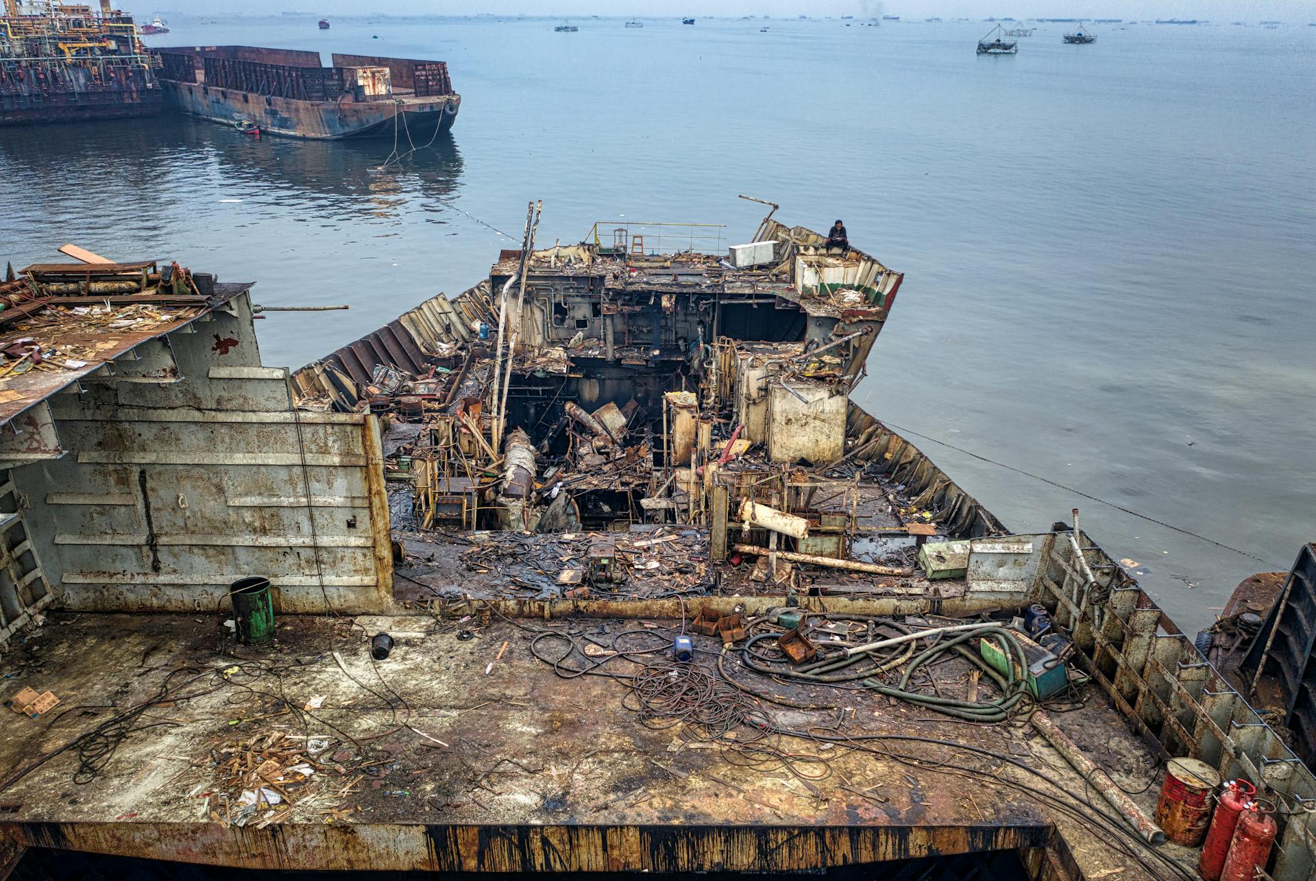 Damaged abandoned rustic ship with garbage moored on dirty shore of ocean in daytime