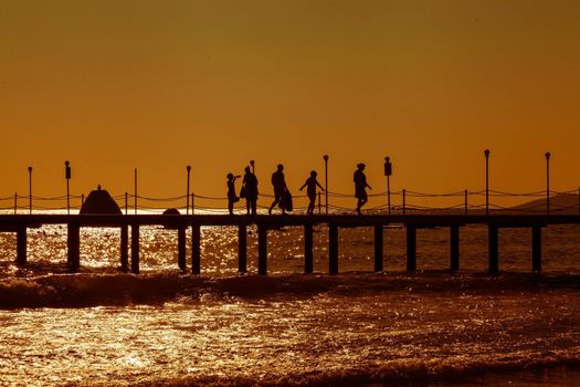 Silhouettes of people walking on a pier during a vibrant sunset over the ocean.