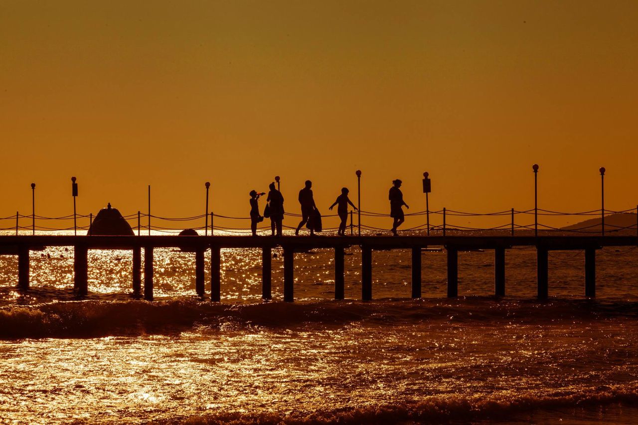 silhouettes of people walking on a pier during a vibrant sunset over t