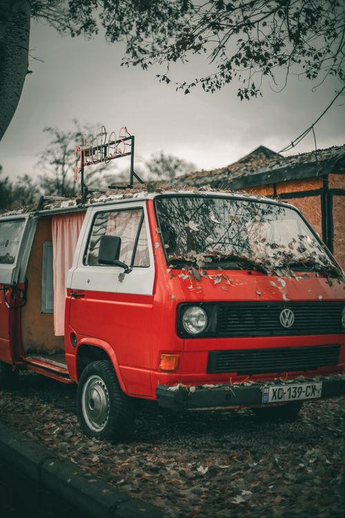 Free Red retro van with opened door parked on yard with fallen leaves on ground near house and tree in daytime in town under gray cloudy sky Stock Photo
