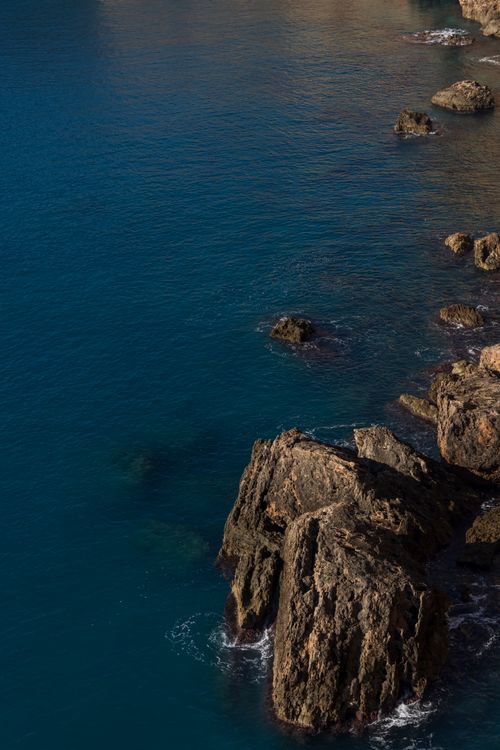 Free Aerial view of rugged rock formations along the ocean coastline under clear skies. Stock Photo