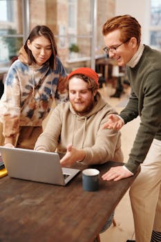 Three colleagues collaborate on a project using a laptop in a cozy office environment.