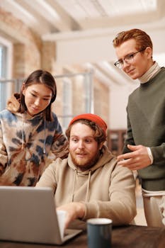 Diverse group of young adults working together on a laptop in a stylish office setting.