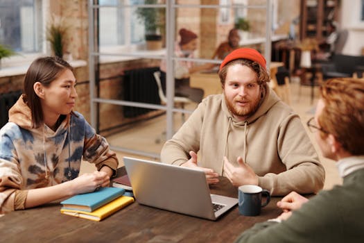 Coworkers engage in a collaborative meeting around a laptop in a modern office setting.