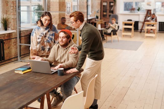 A diverse group of colleagues collaborating around a laptop in a stylish open-plan office.