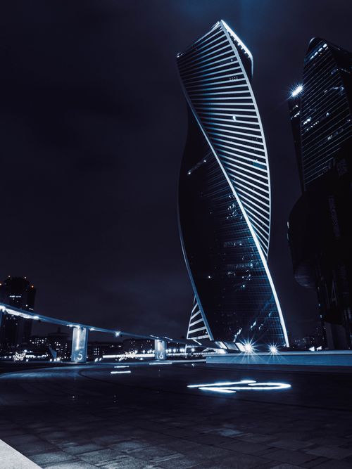 Free A striking view of a modern skyscraper illuminated against Moscow's night sky. Stock Photo