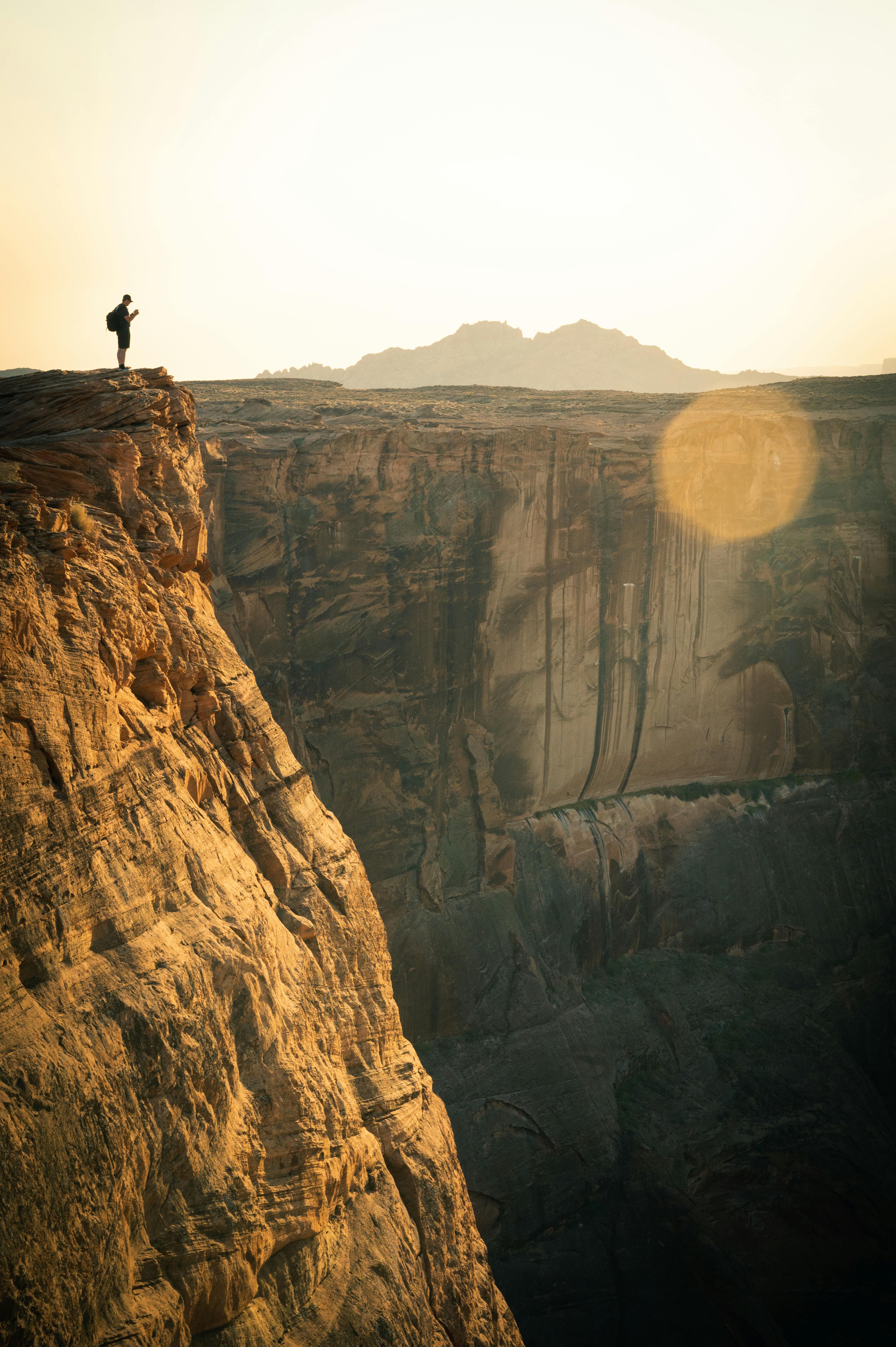 Silhouetted hiker standing on the edge of a canyon in Arizona during sunrise, showcasing stunning geological formations.