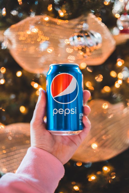 Free Crop unrecognizable person demonstrating bright can of soft drink with cola flavor on shiny blurred background Stock Photo
