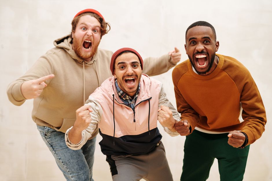 Three diverse men joyfully celebrating together indoors, showcasing friendship and excitement. Three diverse men joyfully celebrating together indoors, showcasing friendship and excitement.