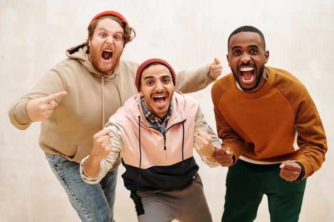 Three diverse men joyfully celebrating together indoors, showcasing friendship and excitement.