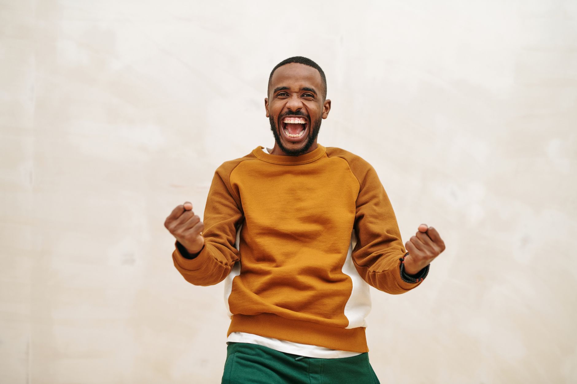 A joyful man with a beard in a sweater, expressing excitement and celebration indoors.