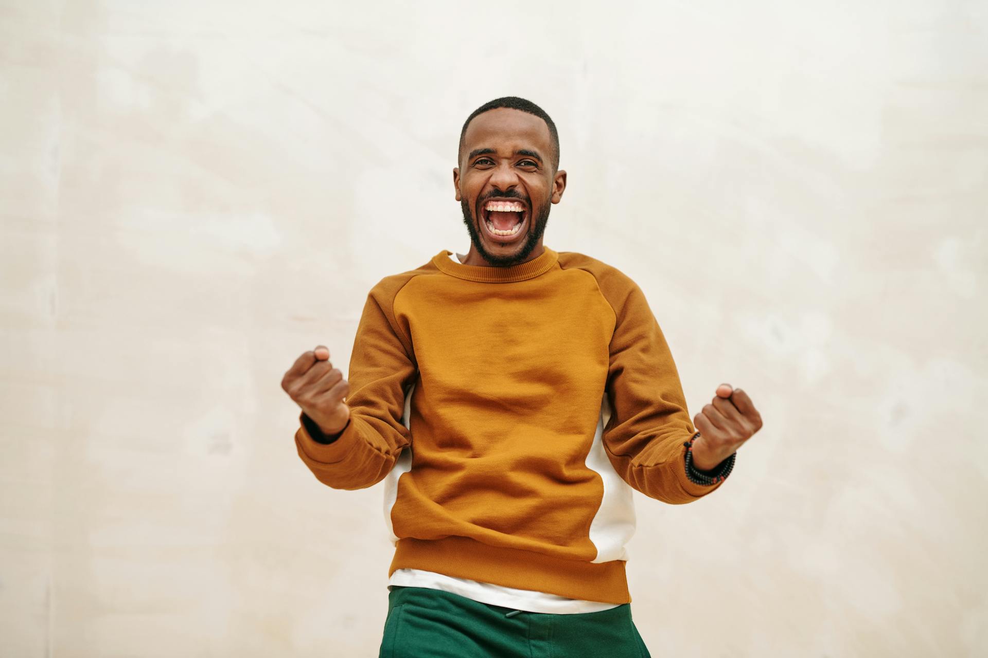 A joyful man with a beard in a sweater, expressing excitement and celebration indoors.