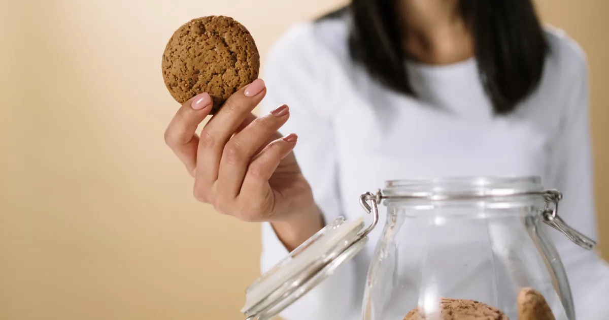 A hand taking a biscuit out of a glass jar