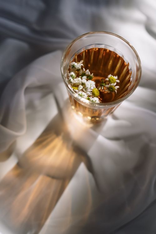 Free A mesmerizing top view of tea in a glass, featuring floating flowers and soft fabric background. Stock Photo