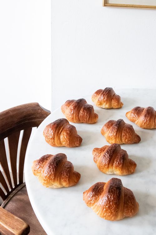 Free Golden croissants lined up on a marble table, perfect for breakfast inspiration. Stock Photo
