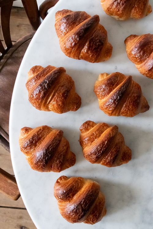 Free Freshly baked croissants arranged on a white marble table, showcasing golden-brown flakiness. Stock Photo