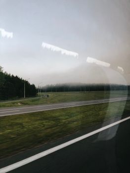 A serene view of an asphalt highway bordered by lush trees, seen through a reflective bus window.