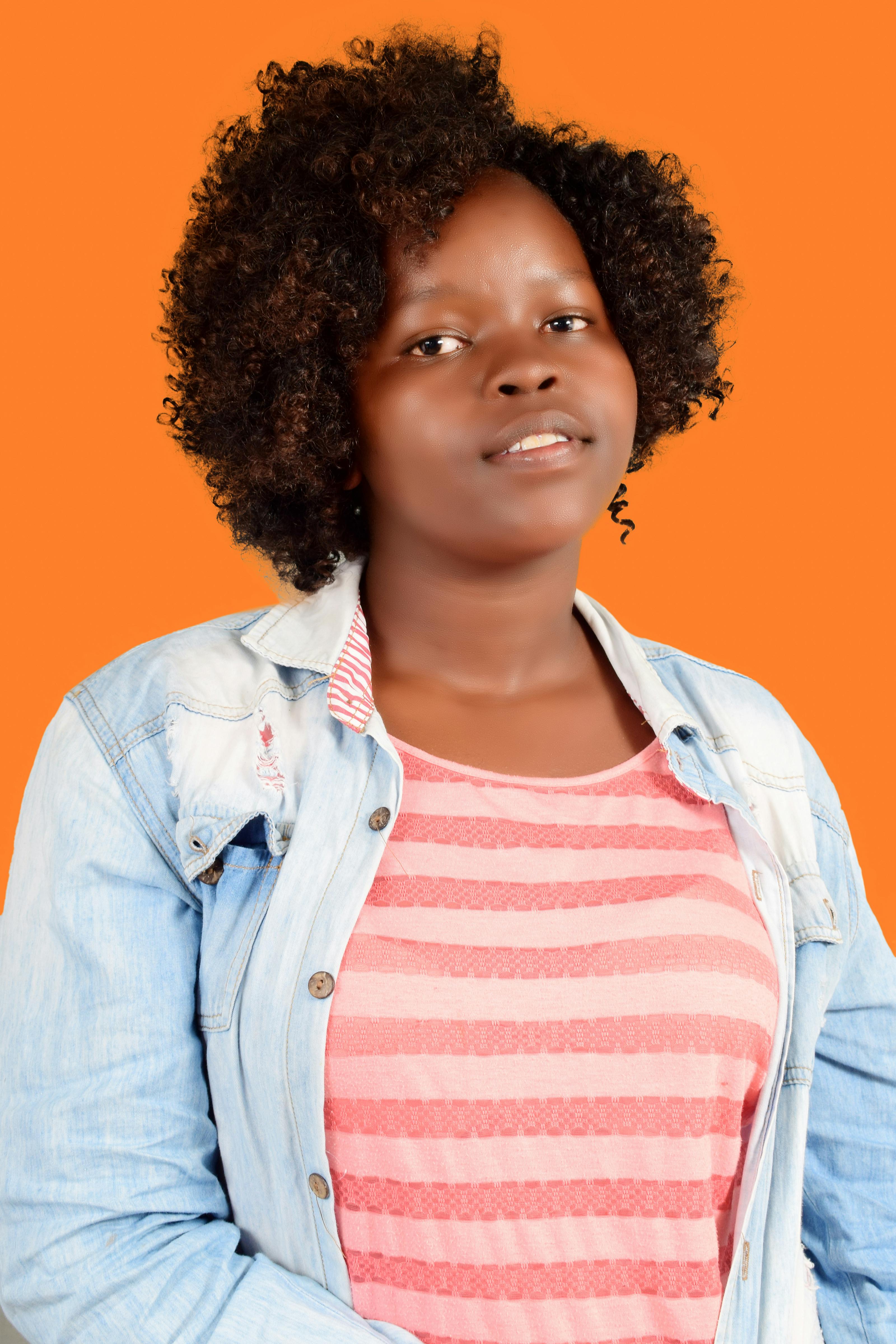 Smiling woman in striped shirt and jean jacket posing against an orange backdrop.